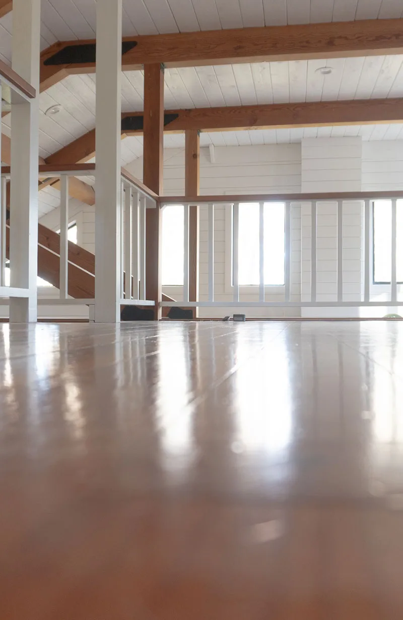 Bright and modern interior featuring polished hardwood floors installed by a skilled flooring installer in Hudson, NC. The space highlights natural wood beams, white railings, and large windows that fill the area with natural light.